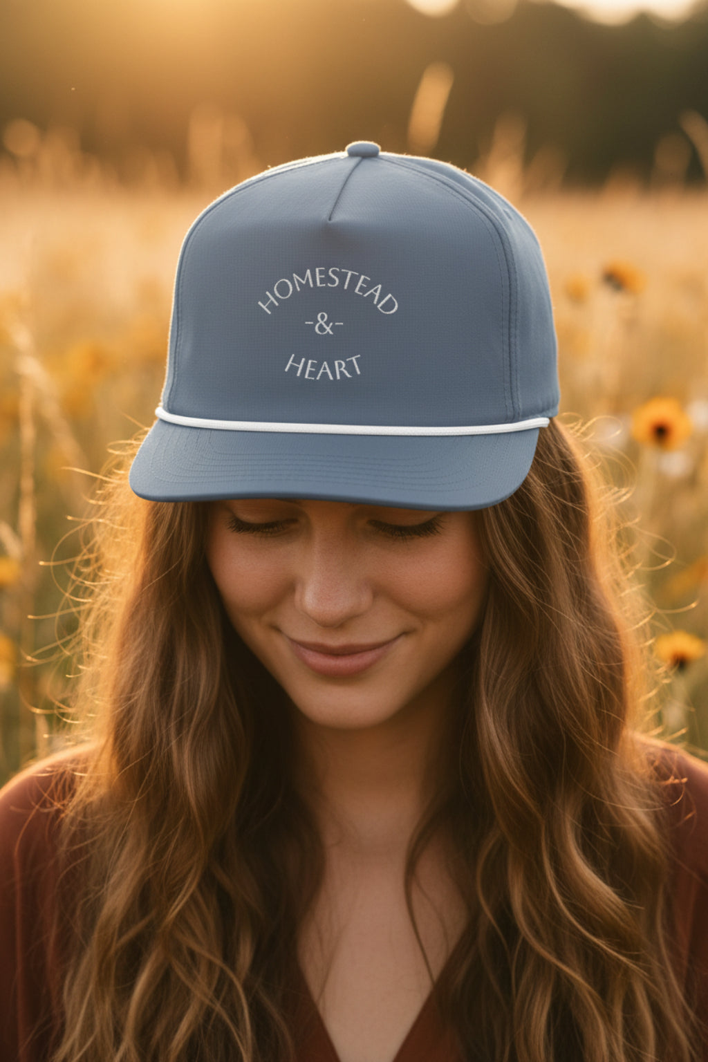 A slate blue snapback cap with a white embroidered logo reading 'HOMESTEAD & HEART' on the front, a white stripe along the brim, and a white button on top, shown against a plain white background.