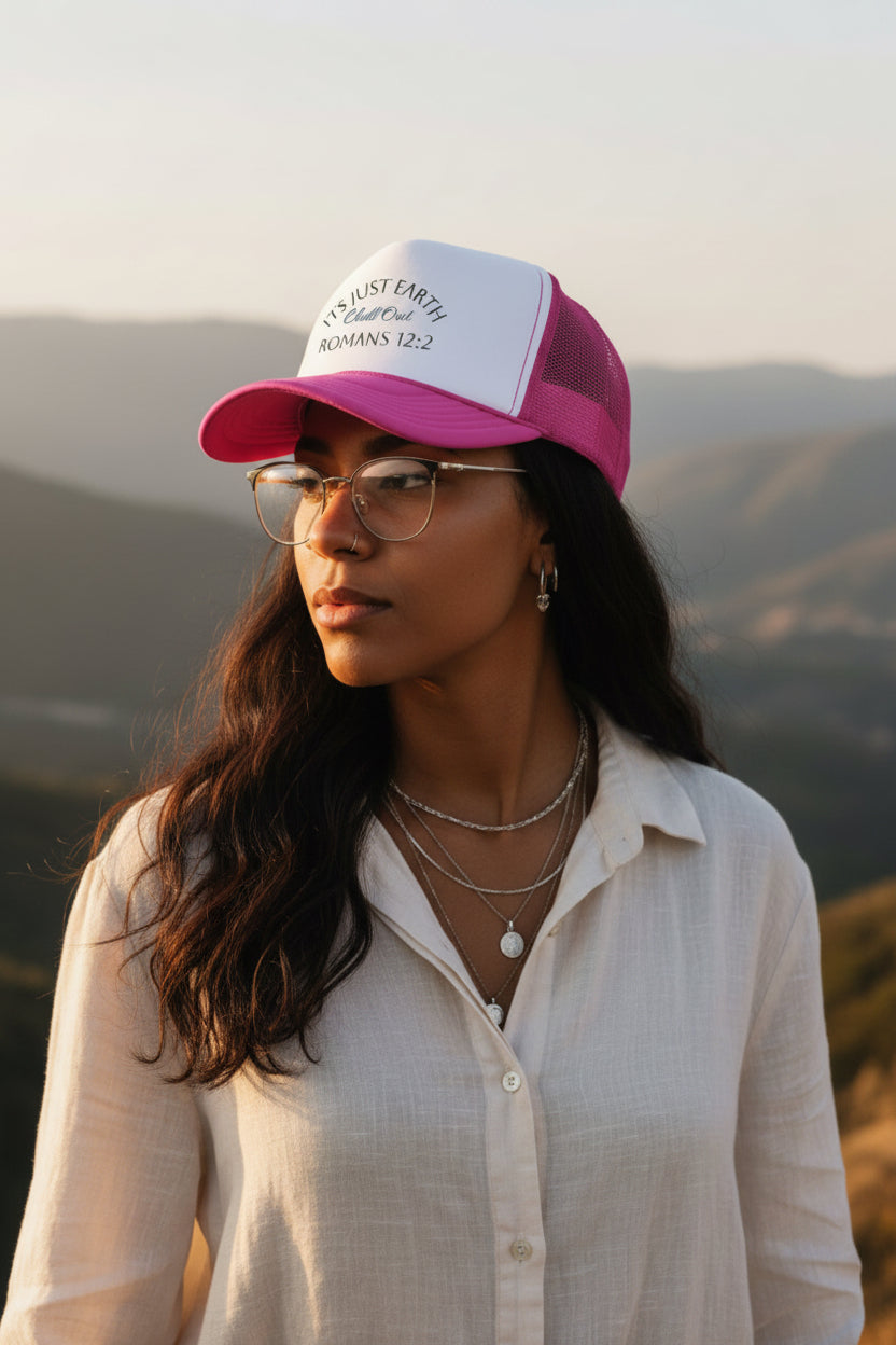 A pink and white trucker hat with the text 'ITS JUST EARTH Chill Out ROMANS 12:2' printed on the front white panel, shown against a plain white background.