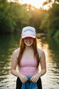 A pink and white trucker hat with the word 'BAPTIZED' embroidered in blue arched letters on the front white panel.