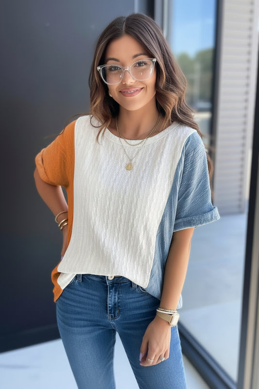 Woman wearing a white top with orange and blue sleeves and denim shorts, standing against a neutral background.