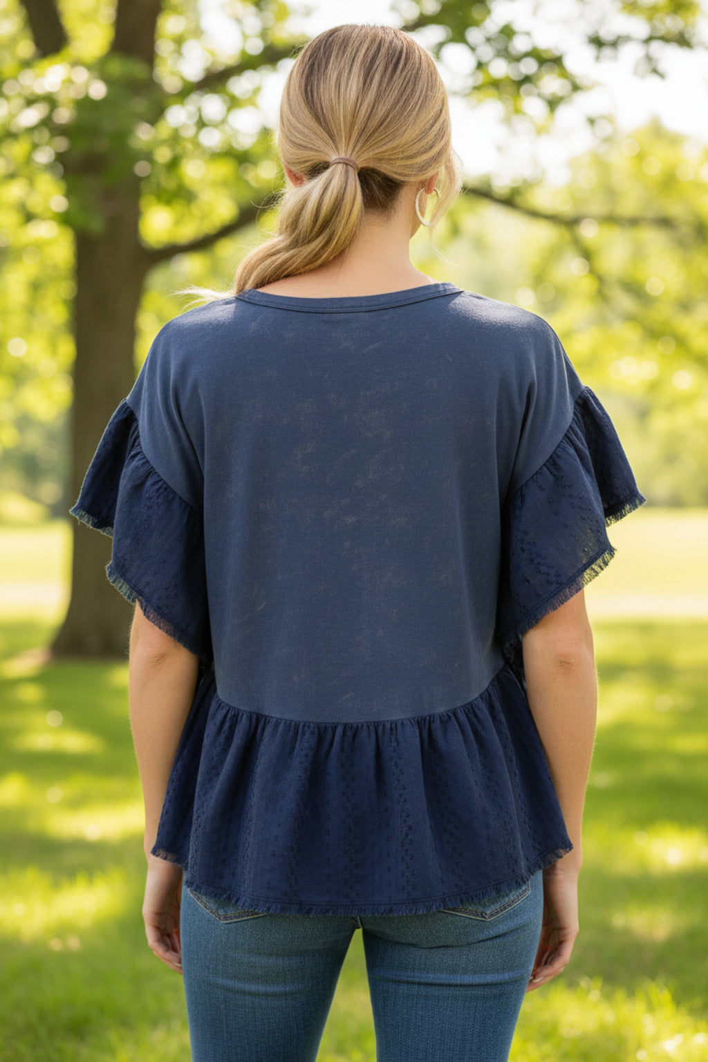 Woman wearing a blue ruffled top and blue jeans with an outdoor background