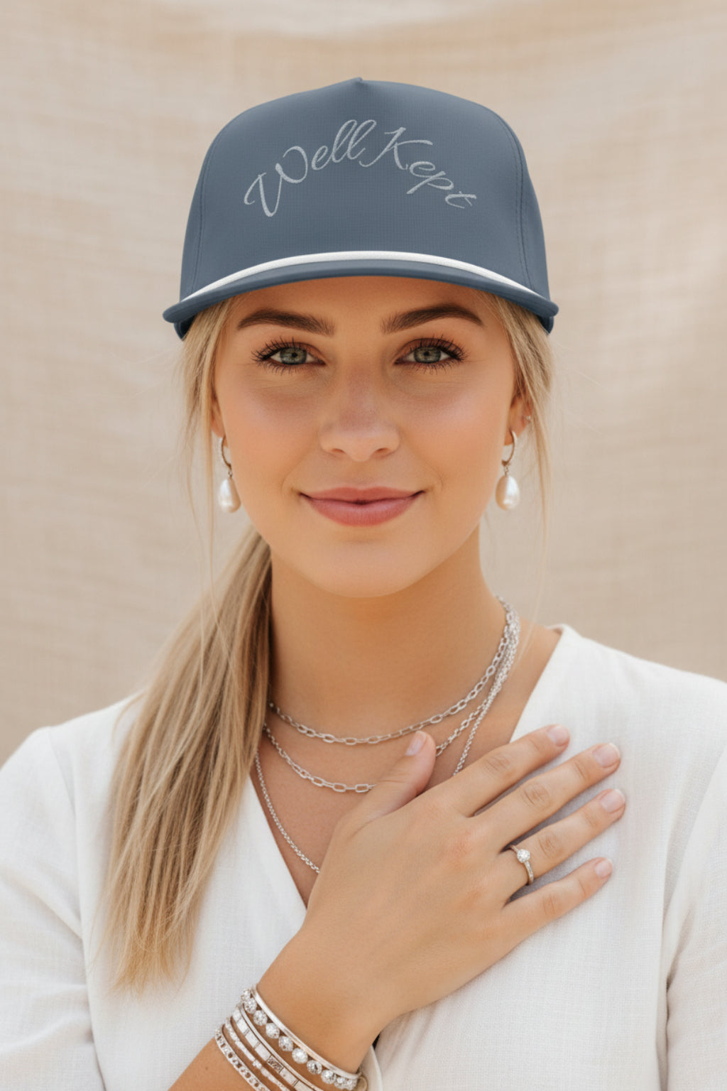 A slate blue snapback cap with 'Well Kept' embroidered in white script across the front, featuring a white stripe along the brim and a matching blue button on top.